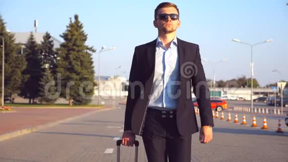 年轻的成功商人戴着太阳镜在日落时带着行李去机场候机楼一个英俊自信的男人视频的预览图