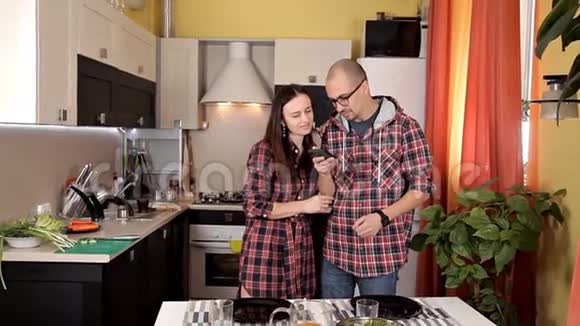 一对年轻夫妇摆好桌子准备晚餐盘子果汁食物在厨房打电话视频的预览图