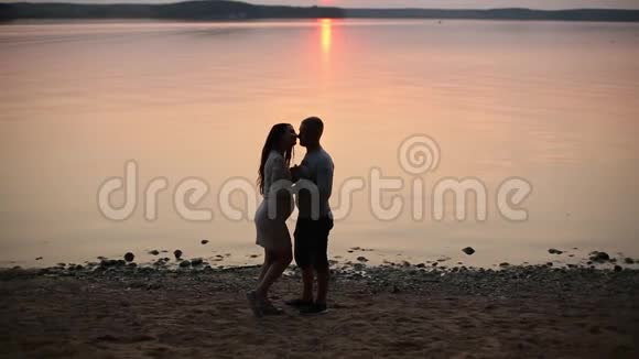 浪漫情侣在湖岸散步日落时接吻的剪影视频的预览图