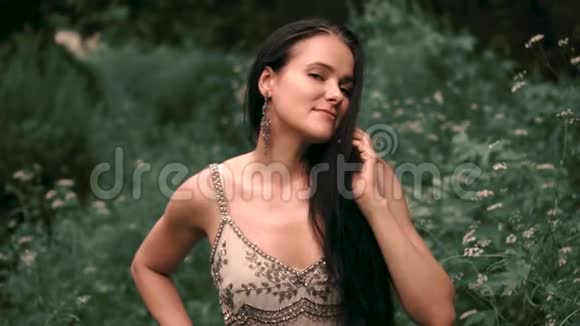一个头发乌黑的女孩穿着一件灰色连衣裙在森林里绣着银绣微笑着对着镜头摆姿势抚摸着视频的预览图