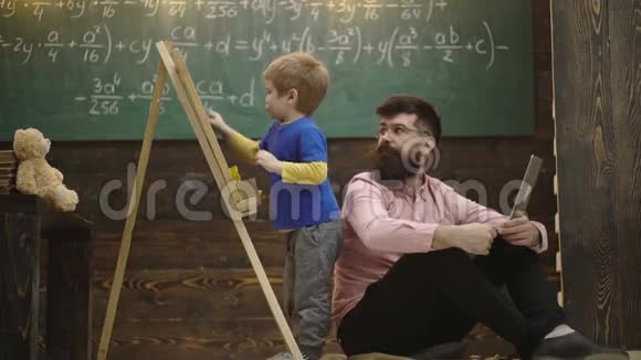 老师检查学生在黑板上写字学生在解决任务时与他的导师或爸爸交谈家庭教育视频的预览图