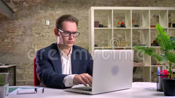 一个穿着黑色西装的严肃的白种人正在做他的工作并深深地思考使用笔记本电脑喝酒视频的预览图