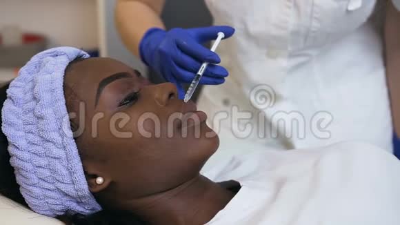 美容师为年轻的非洲女性做美容注射的侧视图视频的预览图