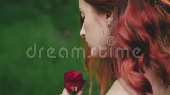 一个红发女孩的肖像从肩膀后面特写一个体贴的女人手里拿着一朵鲜红的玫瑰视频的预览图