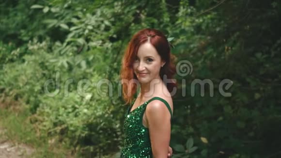 穿着绿色翡翠连衣裙的红发卷曲的女孩微笑着嘲笑相机化妆舞会时尚女郎视频的预览图