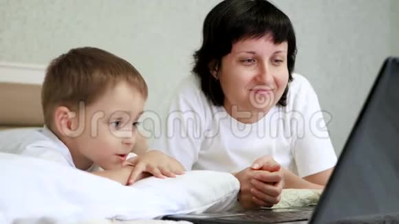 幸福家庭妈妈和孩子躺在床上高兴地看着笔记本电脑屏幕一边互相交谈视频的预览图