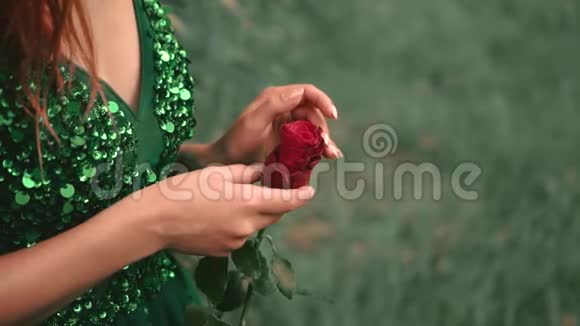 一个在森林里穿着绿色翡翠连衣裙没有一张红卷发的脸的女孩她手里拿着一朵红玫瑰视频的预览图