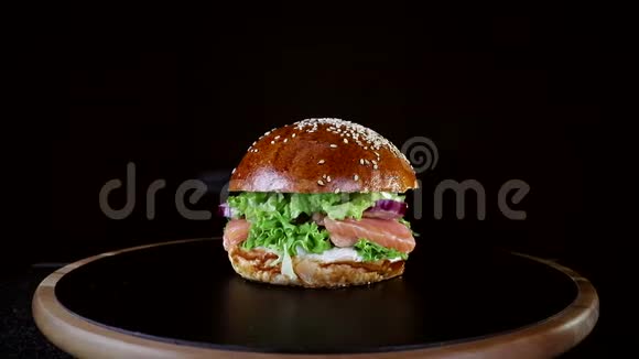 快餐汉堡里有红鱼鲑鱼和鳟鱼西红柿和洋葱在黑色木板上慢慢旋转视频的预览图