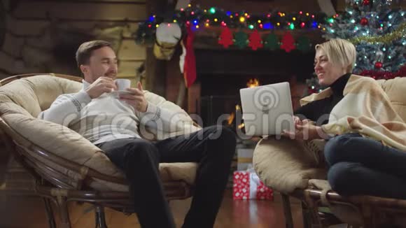 在圣诞节晚上大胡子男人喝着咖啡拿着笔记本跟爱笑的妻子聊天视频的预览图
