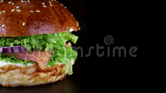 快餐汉堡里有红鱼鲑鱼和鳟鱼西红柿和洋葱在黑色木板上慢慢旋转视频的预览图