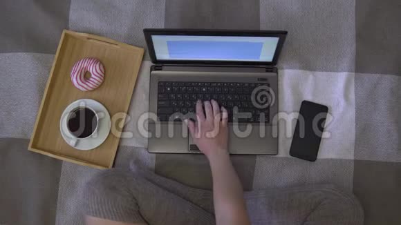 头顶拍摄女孩工作使用笔记本电脑和手机坐在床上在家里喝咖啡4K视频的预览图