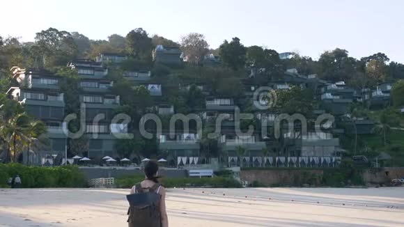 日出时带背包的美丽女游客在海滩上漫步到豪华度假胜地视频的预览图