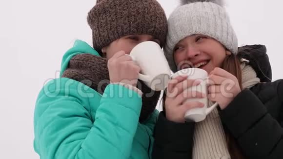 快乐的女孩在冬季公园喝白玻璃咖啡在寒冷的圣诞节妈妈和成年女儿笑了笑视频的预览图