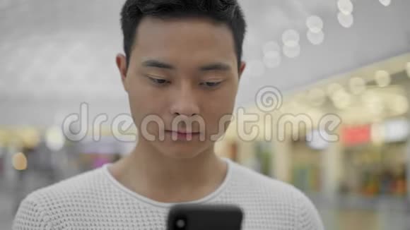 亚洲男性在大型商场背景下滚动手机的肖像画视频的预览图