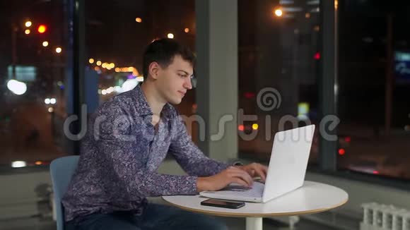 一个男人在笔记本电脑键盘上打字在办公室的一个大窗户里对着夜城视频的预览图