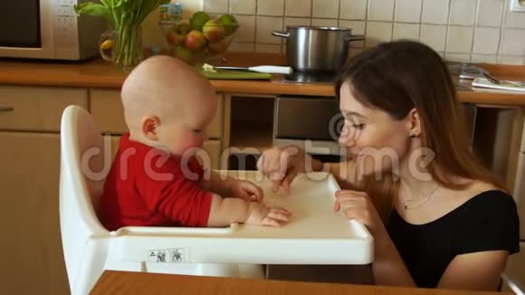 母亲在厨房的高脚椅上喂饥饿的婴儿那女人对婴儿温和地微笑母亲节视频的预览图