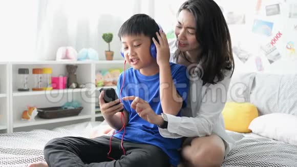 母亲和儿子戴着智能手机耳机在家一起唱歌视频的预览图