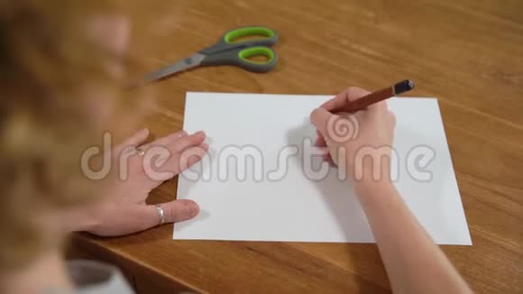 一个年轻的女人在白纸上画一颗心然后用剪刀把它剪下来为爱制作礼物视频的预览图