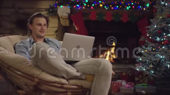 圣诞夜年轻英俊的壁炉架在笔记本电脑上开着摄像机视频的预览图