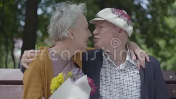 成年妇女抱着一束美丽的花而她年迈的丈夫拥抱着她温情的成年夫妇视频的预览图