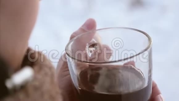 在寒冷的冬日女孩从玻璃杯里喝着热腾腾的美味茶特写镜头视频的预览图