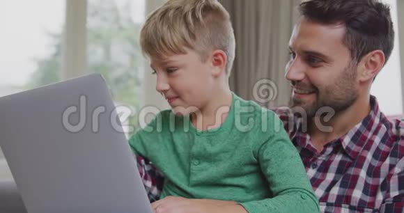 父子俩在舒适的家里用笔记本电脑视频的预览图
