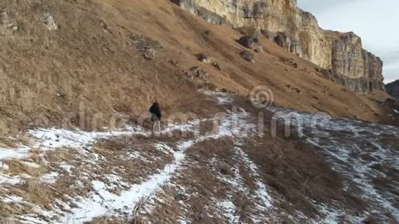 穿着羽绒服和帽子的女游客在岩石峡谷的初冬沿着小径散步黄色的草和碎片视频的预览图