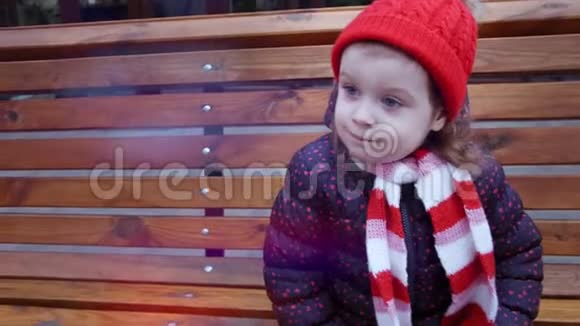 冬天坐在城市公园的长凳上的小可爱的微笑女孩视频的预览图