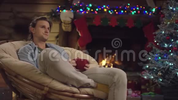 长头发的帅哥在圣诞夜用装饰的树喝茶视频的预览图