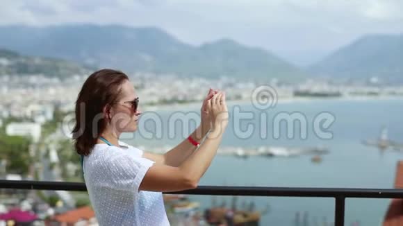 一位穿着白色连衣裙的女游客在智能手机上从鸟瞰拍摄城市的照片城市的景色视频的预览图
