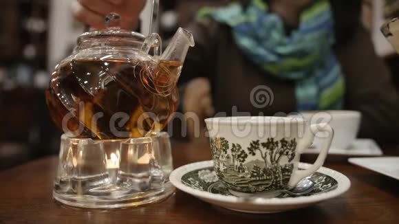 靠近玻璃茶壶的镜头站在玻璃底座上里面有一支蜡烛手在往杯子里倒茶视频的预览图