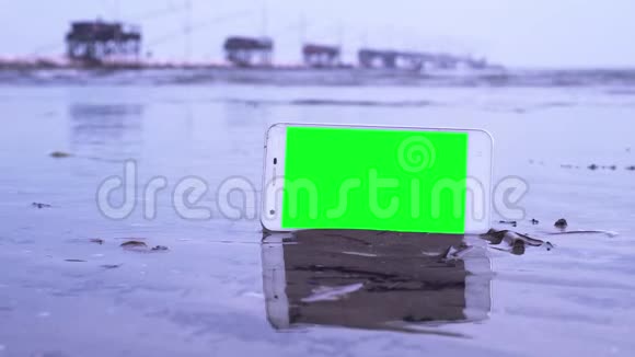 沙滩上有绿色屏幕的智能手机沐浴在海水中视频的预览图