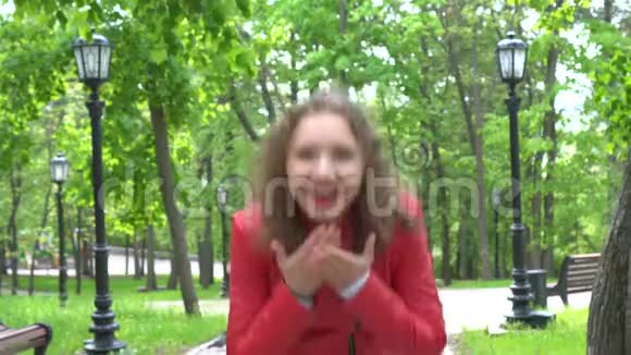 穿着红色皮夹克的令人惊讶的女人看着相机惊讶地在户外度过夏天的公园视频的预览图