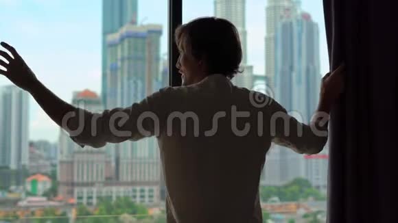 一个男人的剪影用摩天大楼把俯瞰市中心的窗户的窗帘拉上视频的预览图