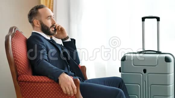 在商务旅行中微笑男商人与使用智能手机的伙伴交谈视频的预览图