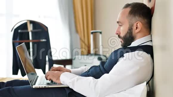 中长型年轻男性商人坐在酒店床上使用笔记本电脑浏览网页视频的预览图