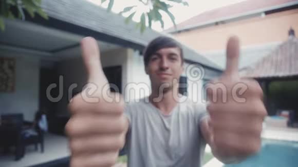 快乐的年轻人竖起两个大拇指微笑着在房子前面视频的预览图