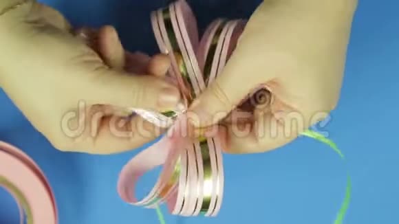女人双手系着粉红色的辫子粉红色的空白作为礼物蝴蝶结蓝色背景视频的预览图
