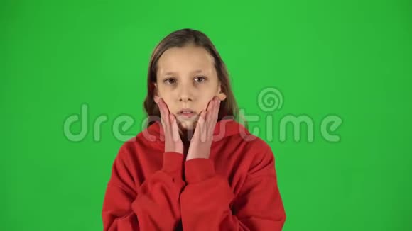 小女孩害怕把脸藏在绿色背景的工作室里视频的预览图