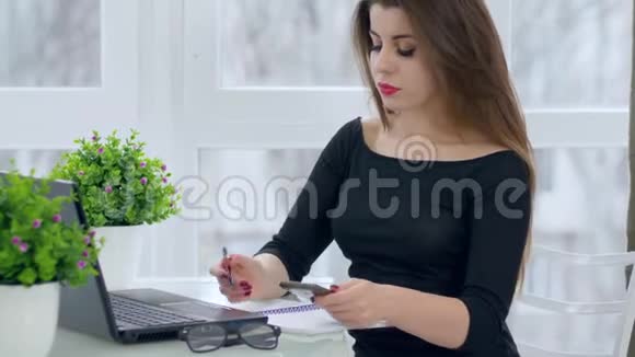 成功的人长发女孩在工作中使用笔记本电脑和移动电话坐在办公桌旁的轻型办公室里视频的预览图