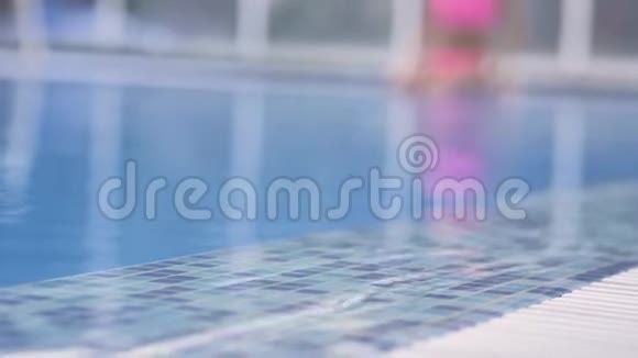 穿着粉红色泳衣的金发美女在一个清澈的蓝水池里游泳视频的预览图