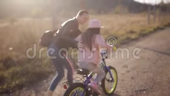 妈妈教小女孩在温暖的秋夜骑自行车幸福家庭的概念视频的预览图
