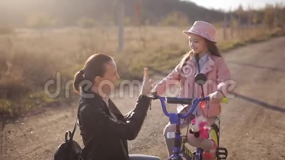 妈妈教小女孩在温暖的秋夜骑自行车幸福家庭的概念视频的预览图