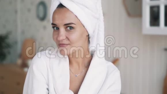 穿着浴袍头上戴毛巾的女人的肖像看着镜头微笑慢动作视频的预览图