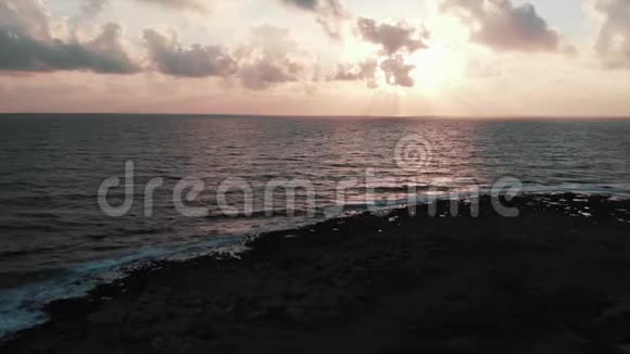 一张美丽的粉红色日落海浪拍打着岩石海滩视频的预览图