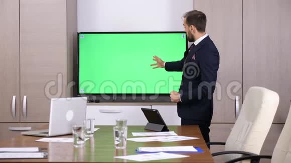 会议室里的商人指着一台绿色屏幕模拟电视视频的预览图