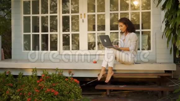 一位年轻漂亮的女性自由职业者正坐在露台上在她家的背景一台笔记本电脑视频的预览图