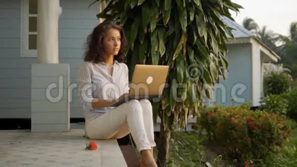 一位年轻漂亮的女性自由职业者正坐在露台上在她家的背景一台笔记本电脑视频的预览图