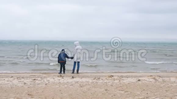 妈妈和儿子在冬天的海边沙滩上散步后景美丽的沙和雪风暴的景色视频的预览图