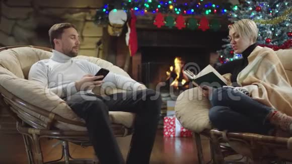 圣诞之夜快乐的一对夫妇在看书和使用智能手机时聊天视频的预览图